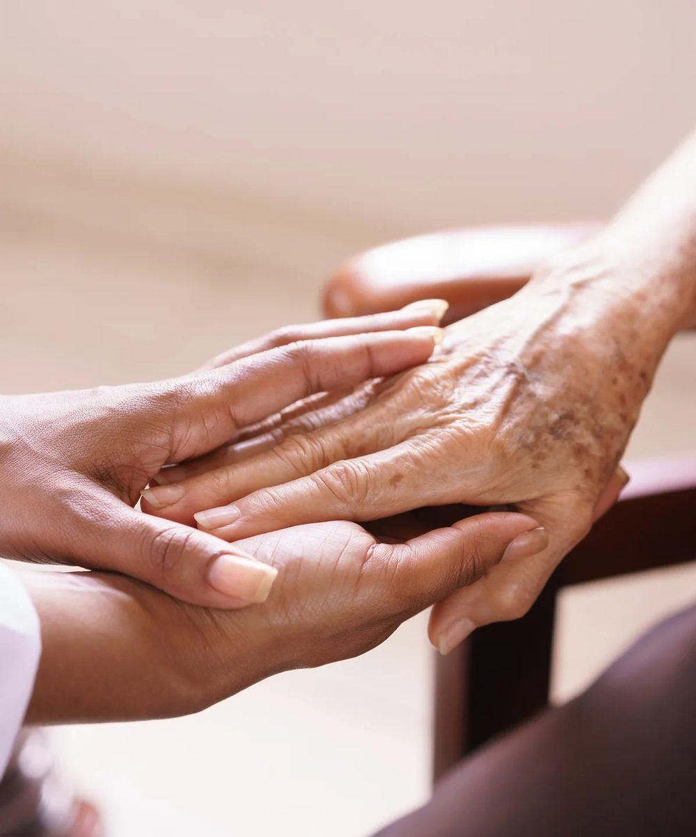 A caregiver gently holding an older woman's hand